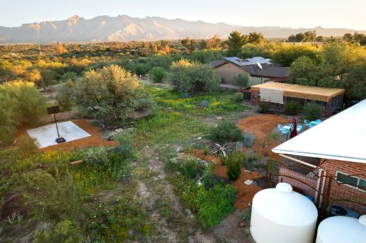 view from above of a property with two large white rainwater tanks, a garden, native plants, and solar panels