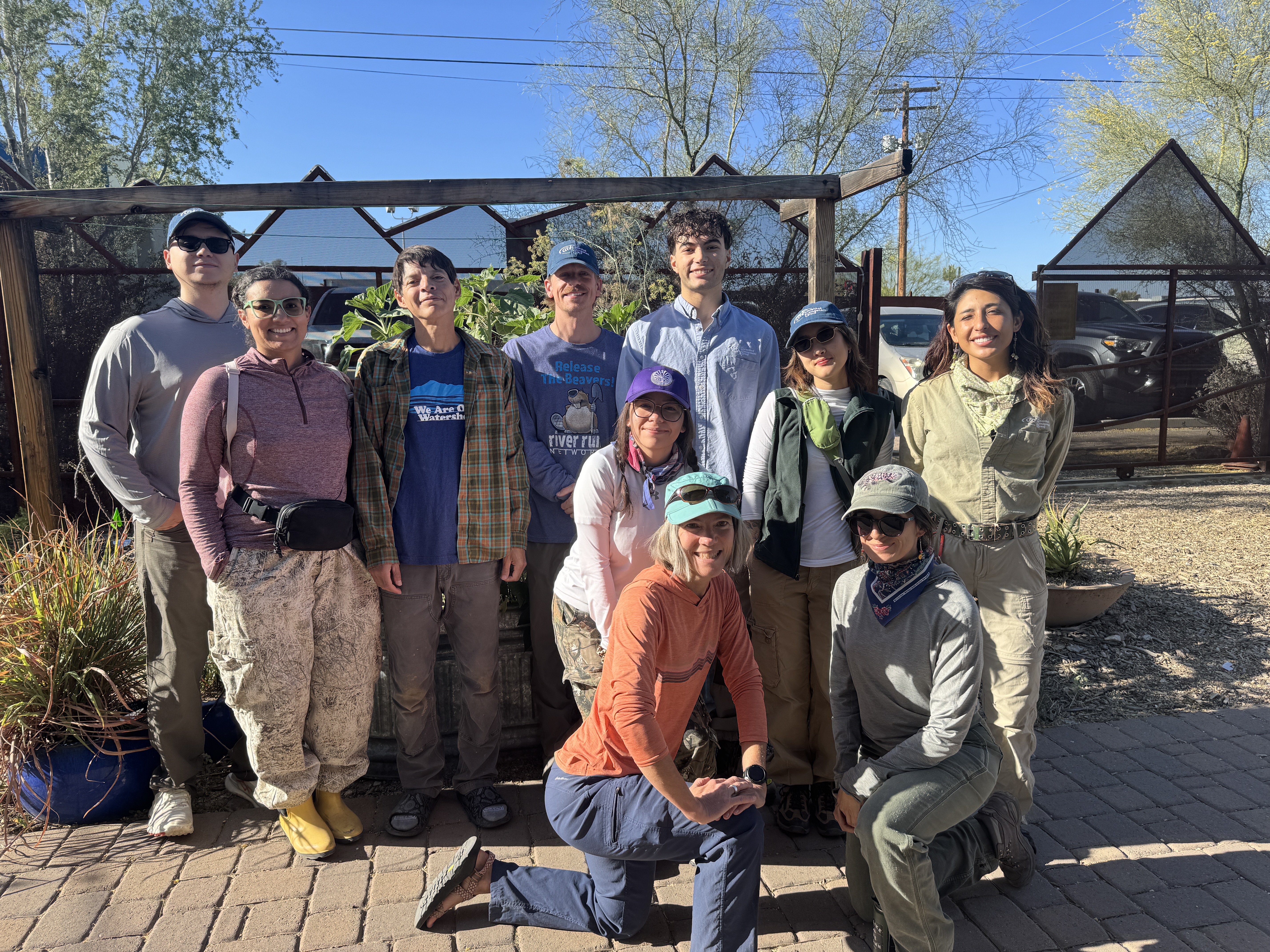 A smiling group of staff, apprentices, interns, and docents posing in front of a rain garden at the Living Lab