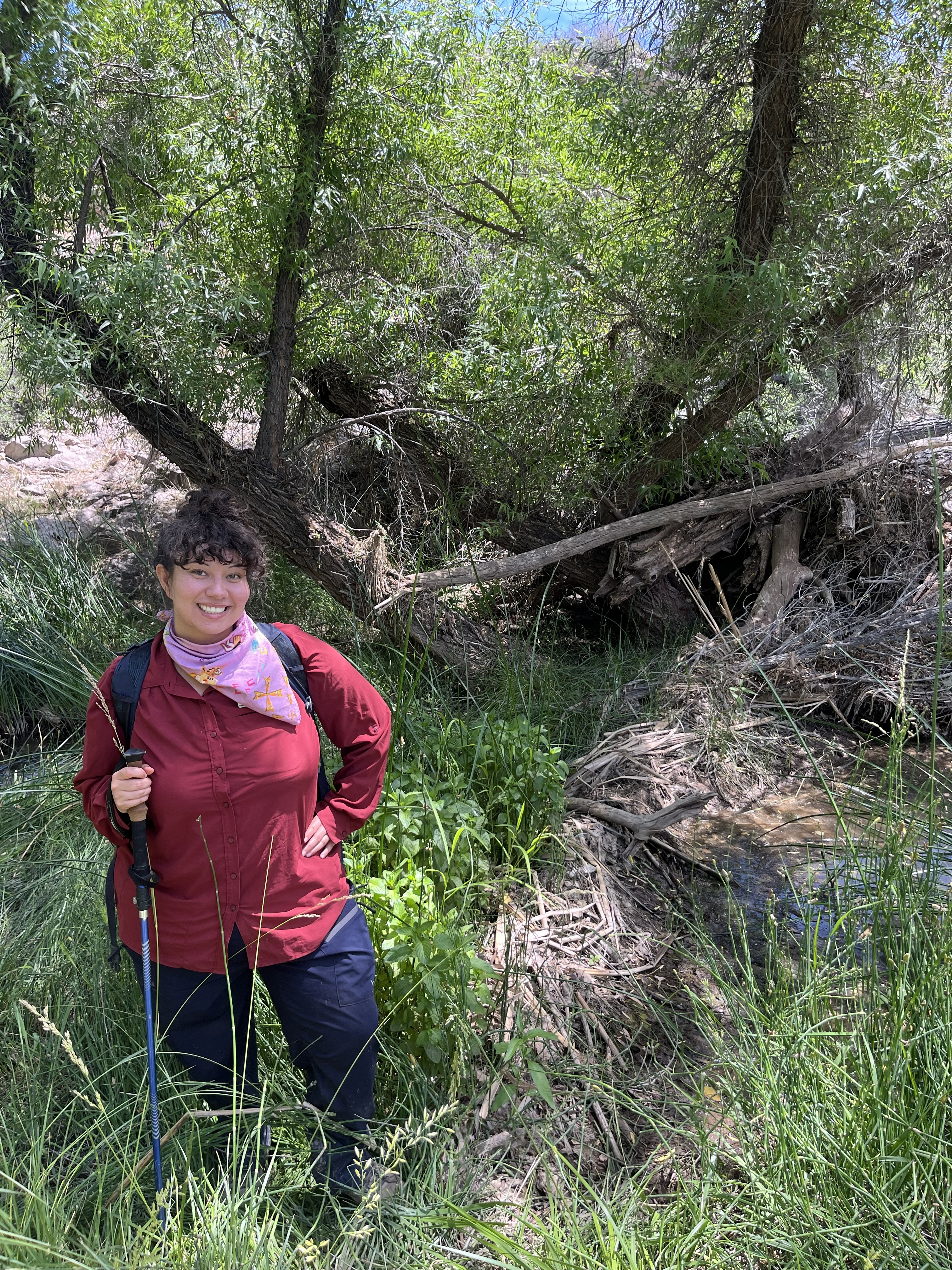 The blog's author, Nadira, standing in field clothes next to a beaver dam and smiling