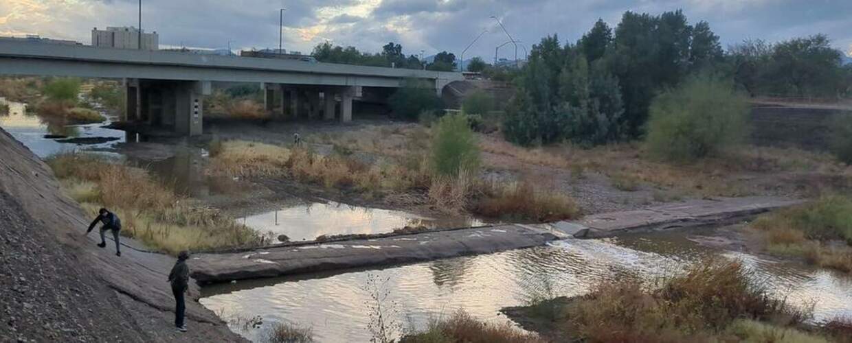 creek flowing through a spillway in a low dam as two people climb the concrete banks