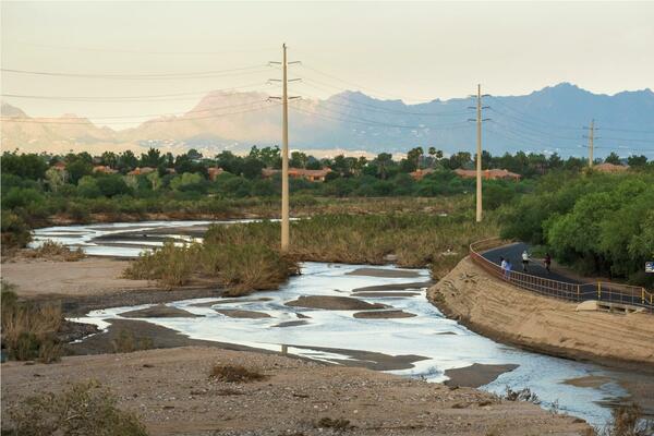 Meandering water flows in a river bed in front of mountains. Power lines run through the river bed